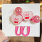 Heart-shaped hair clips with cherry design on a white card, held by a hand.