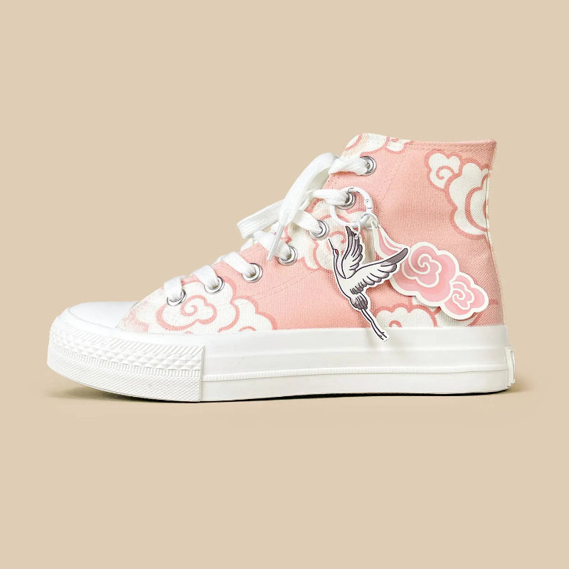 A pink high-top canvas sneaker with white laces, a white rubber sole, and a white cloud pattern. It features a silver metal bird charm hanging from the lace loop, set against a solid beige background.