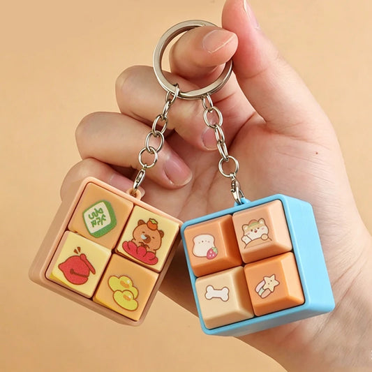 Two colorful keychains with cartoon designs held by a hand against a beige background
