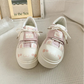 Pair of cute cat pink and white sneakers with paw print designs on a textured surface.