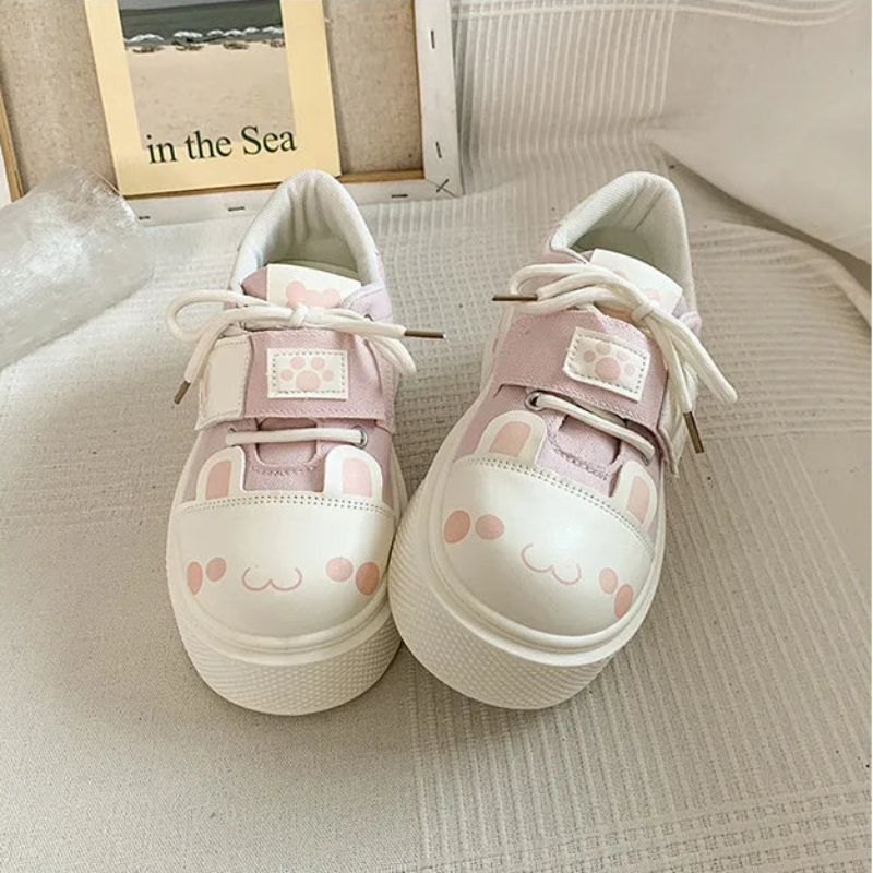 Pair of cute cat pink and white sneakers with paw print designs on a textured surface.