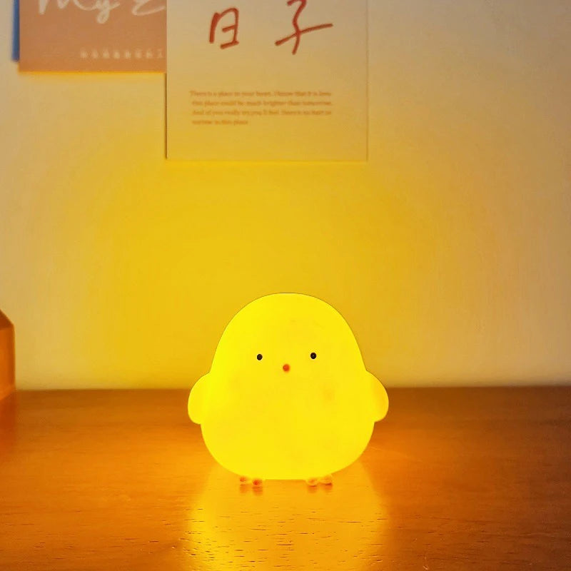 Yellow chick-shaped night light on a wooden surface with a warm glow.