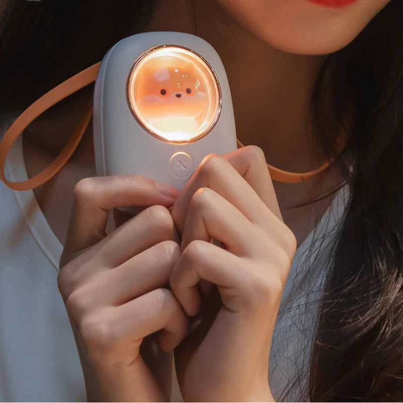 Person holding a small, round, white shiba inu device with a glowing orange light.
