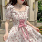 Woman wearing a floral dress with a pink ribbon in an outdoor setting