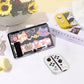 Gaming console with cartoon cat design on screen, surrounded by decorative items including a yellow flower arrangement and a magazine.