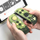 Green and black game controllers with cartoon paw prints held by hands, with a computer screen in the background.