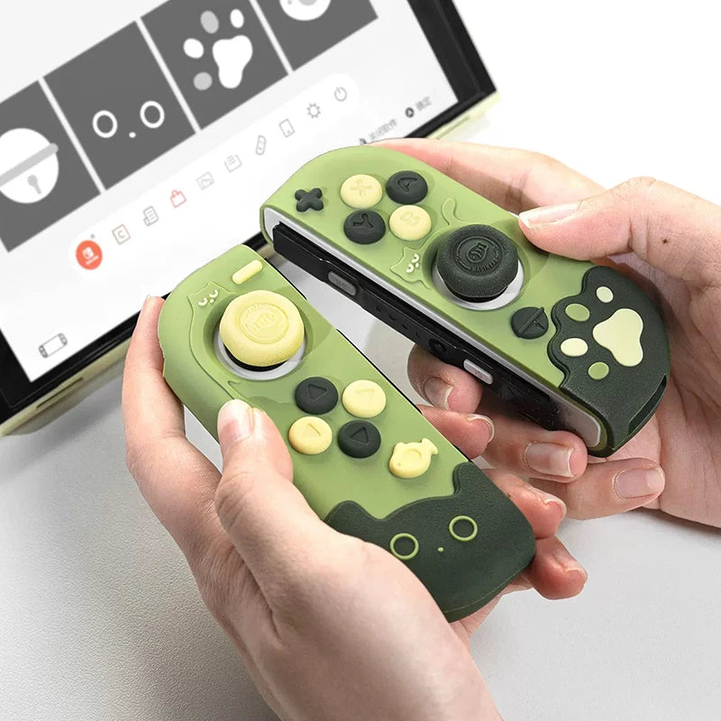 Green and black game controllers with cartoon paw prints held by hands, with a computer screen in the background.