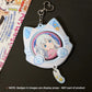 A light blue and white cat-shaped keychain featuring an anime character badge in the center, displayed on a dark surface next to its printed packaging card.