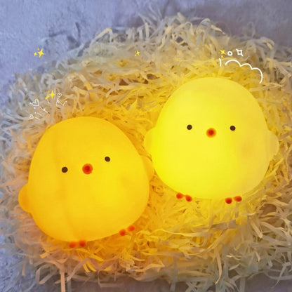 Two yellow chick-shaped lights on a bed of straw with decorative elements.