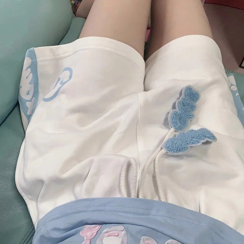 White shorts with light blue cartoon graphics and a blue textured applique detail, worn by a person sitting on a mint green couch.