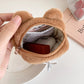 Brown bear-shaped pouch with a hand holding it open, revealing items inside.