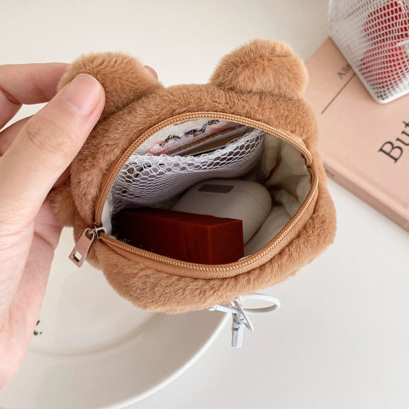 Brown bear-shaped pouch with a hand holding it open, revealing items inside.