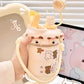 Cute water bottle with bear designs held by a hand, with a soft toy in the background.