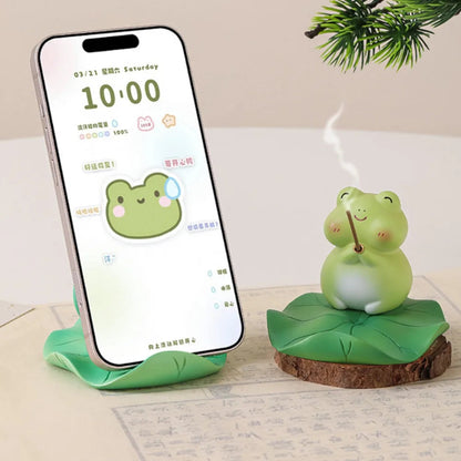 Smartphone on a stand with a frog-themed device next to it on a light surface.