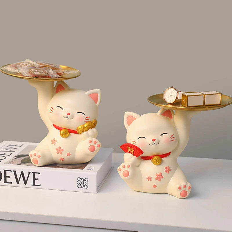 Two decorative cat figurines with trays on a neutral background