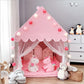 Pink children's play tent with toys and string lights in a room.