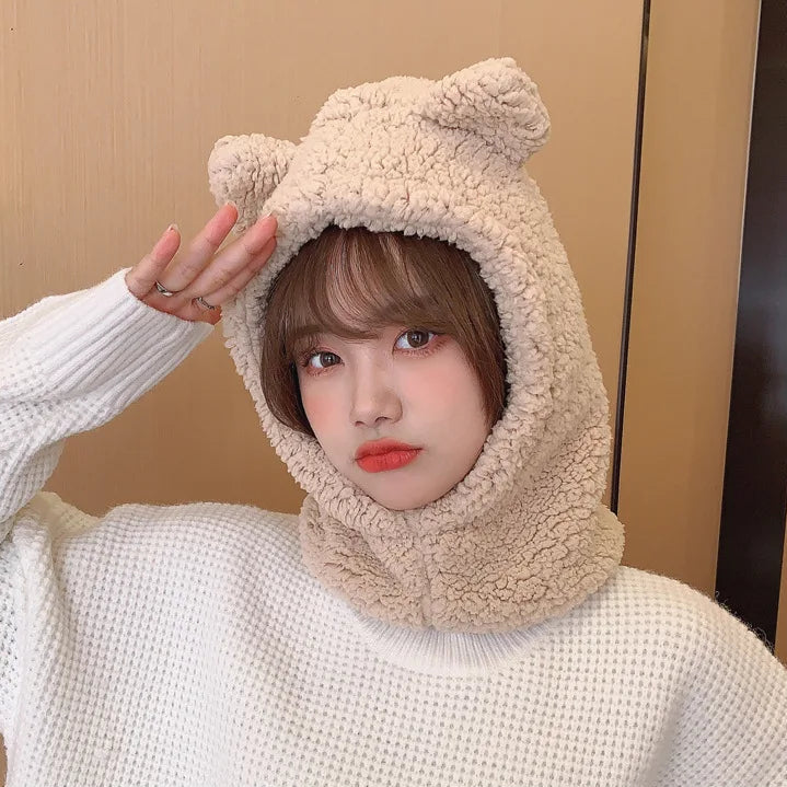 Person wearing a beige fleece hat with bear ears against a beige wall.