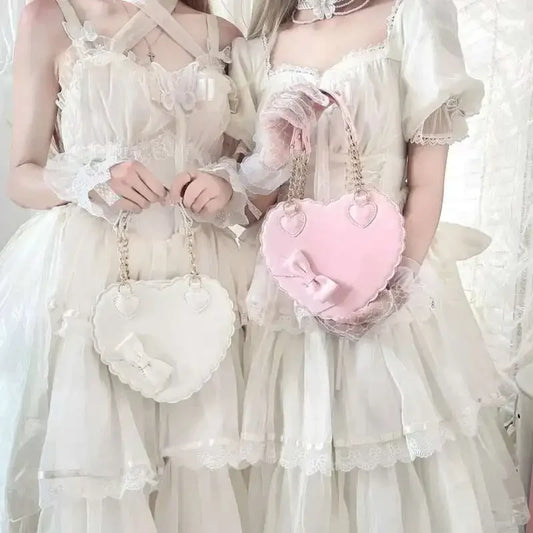 Two women in vintage-style dresses holding a white handbag and a pink heart-shaped bag.