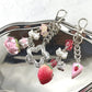 Keychain with various charms including a strawberry, heart, and flower on a reflective surface.