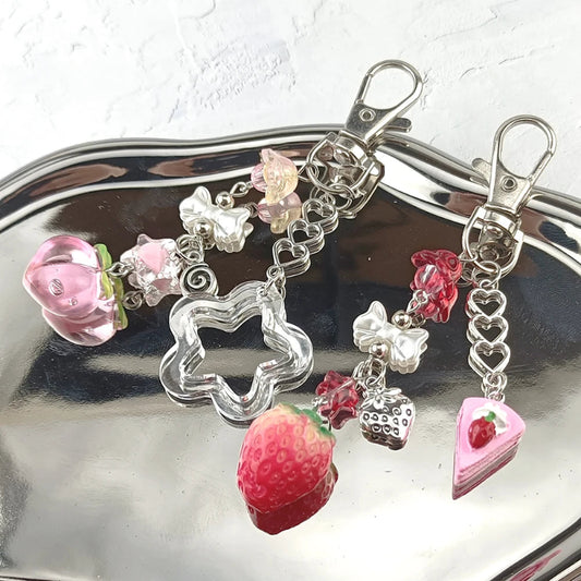 Keychain with various charms including a strawberry, heart, and flower on a reflective surface.
