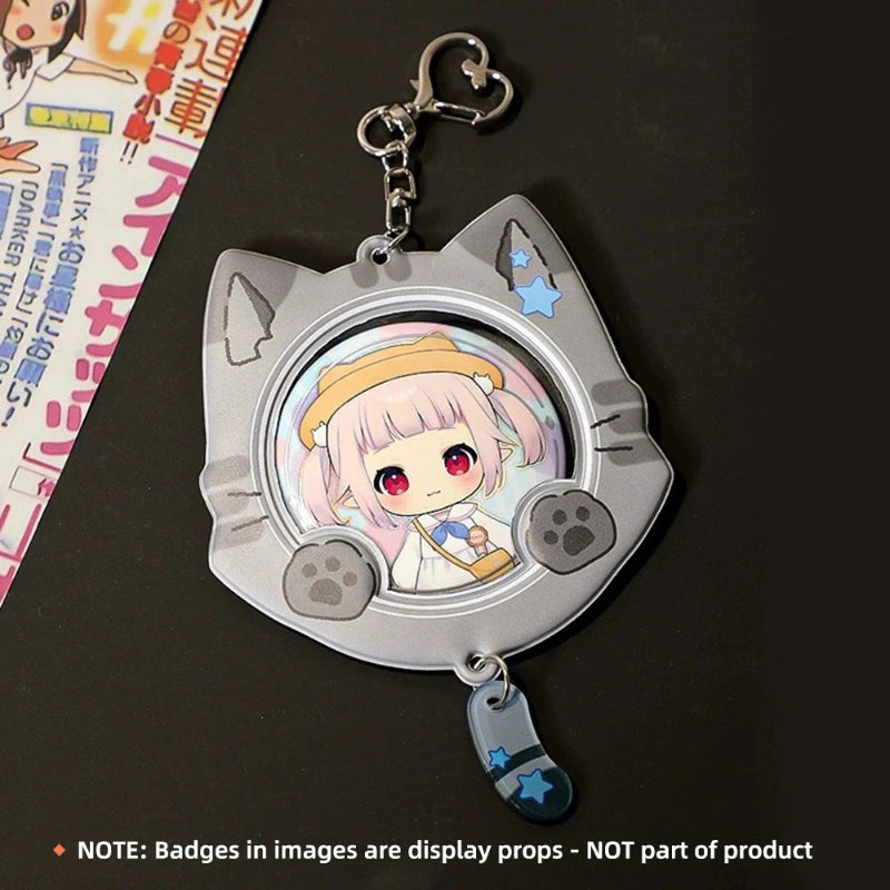 A silver cat-shaped keychain with paw prints and a chibi anime character display window, shown on a dark surface with a printed card partially visible on the left. A note at the bottom clarifies that the display badges are not part of the product.