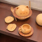 A cute cat-themed dinnerware set on a dark wooden table, featuring a cat-shaped bowl with chopsticks, matching plates, a small cup, and a spherical container, all in a warm pastel peach and orange color scheme.