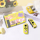 Yellow gaming console with cat-themed design on a white surface with a magazine and flowers in the background.