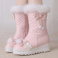 Pink winter boots with white fur lining and decorative bows on a neutral background