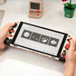 Handheld gaming console with colorful buttons held by a person on a light surface.