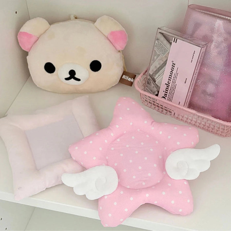 Pink star-shaped coaster with angel wings on a shelf with a plush toy and box.