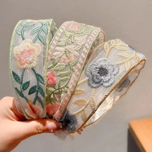 Three floral cottagecore embroidery headbannds held by a hand against a neutral background