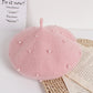 Pink beret with pearl embellishments on a white surface with text and an open book.