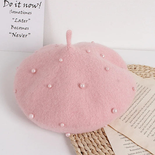 Pink beret with pearl embellishments on a white surface with text and an open book.
