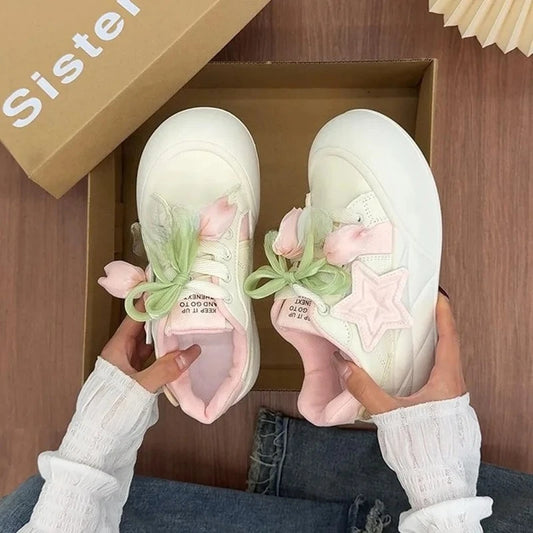 Pair of pastel-colored sneakers with decorative elements held by a person, with a box labeled 'Sister' in the background.