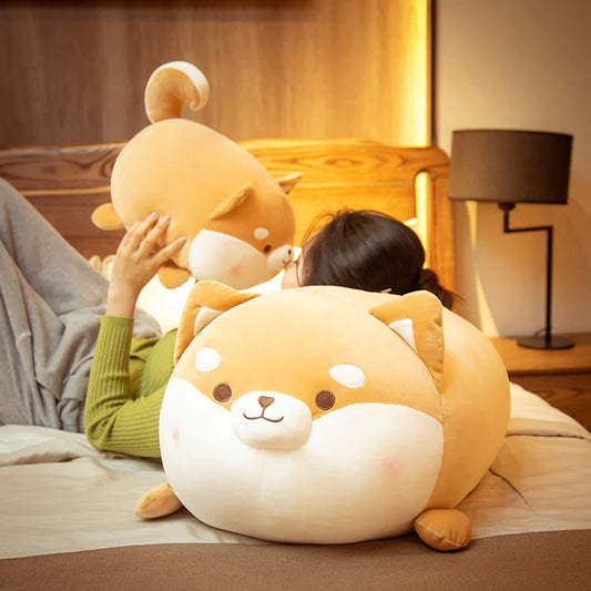 Person holding a large plush dog toy on a bed in a cozy room.