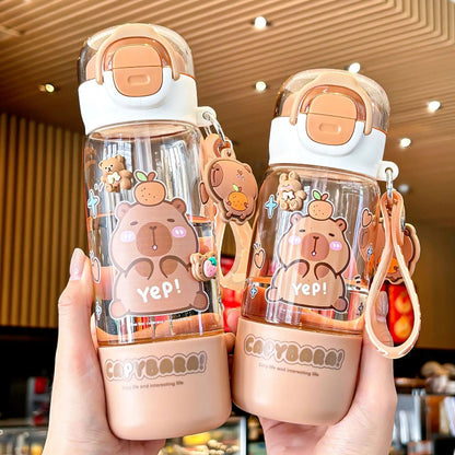 Two Capybara themed water bottles held by a person in an indoor setting.