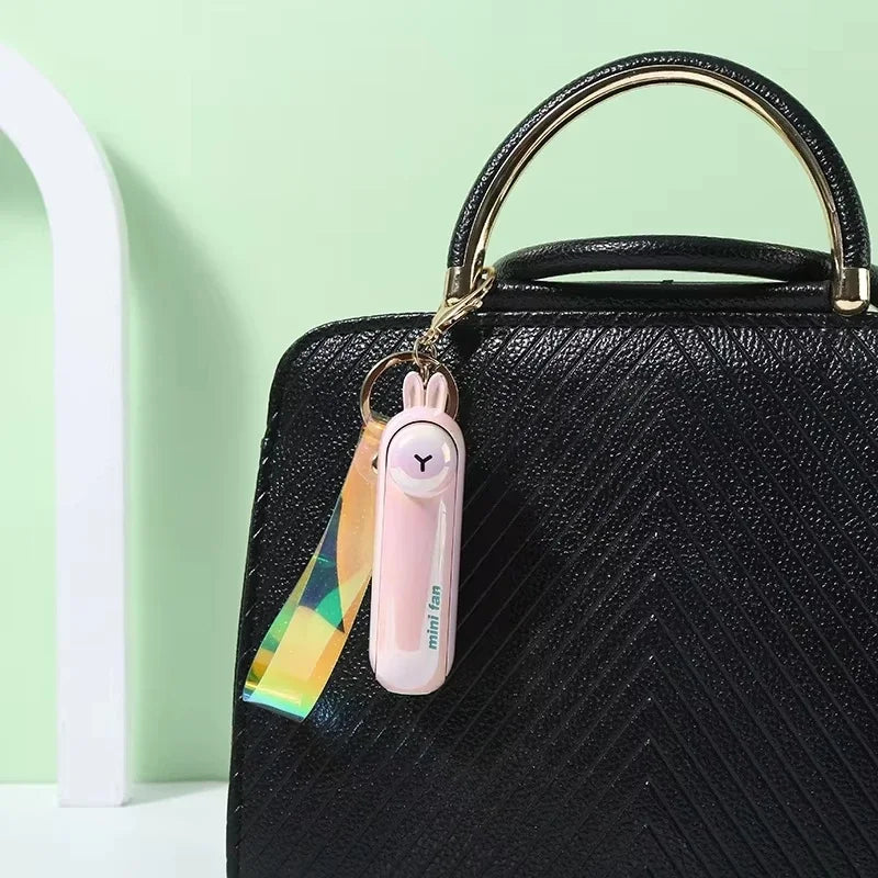 Pink fan with colorful strap attached to a black handbag against a light green background