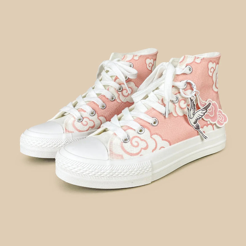 A pair of high-top canvas sneakers in light pink with white cloud patterns, white laces, and white rubber soles. One shoe features a silver metal bird charm.