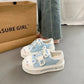 Pair of cute cat light blue and white sneakers with cartoon designs on a gray floor, next to a cardboard box with 'ASURE GIRL' branding.