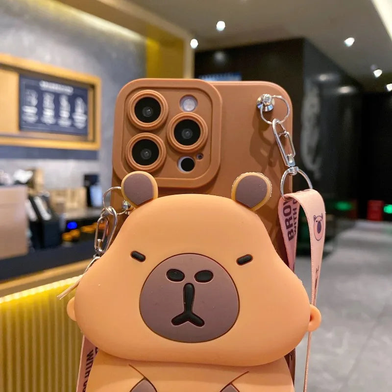 Light brown Capybara-shaped phone case with a strap in an indoor setting