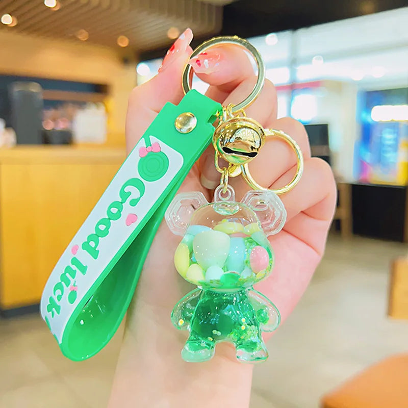 Green keychain with a small bear-shaped charm held by a hand in an indoor setting.