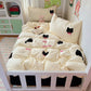 A cozy children's bedding set styled on a white wooden bed frame, featuring a cream-colored duvet cover and matching pillowcases decorated with black cat faces and pink bows, alongside a small plush bunny.