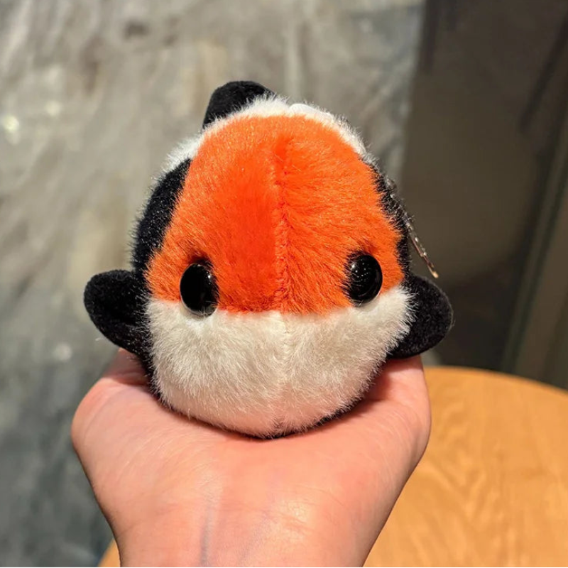 Plush koi fish with orange face, black fins, and white body held in a hand.