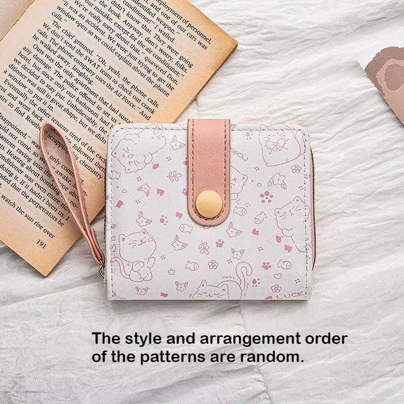 Small pink wallet with cat pattern on a white surface with an open book