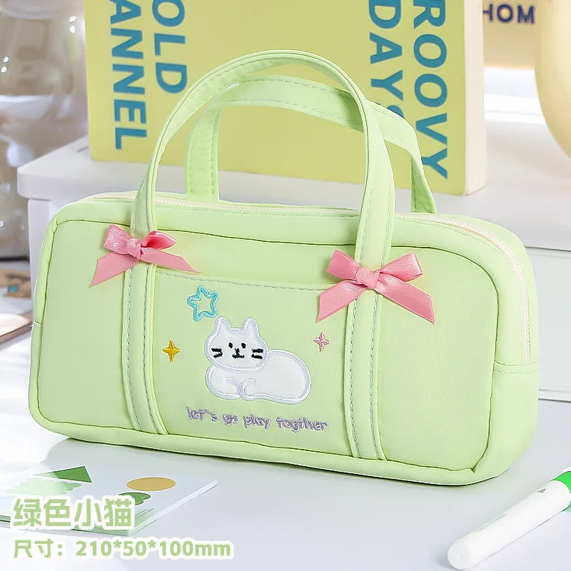 Light green pencil case with cartoon cat design and pink bows on a white surface.