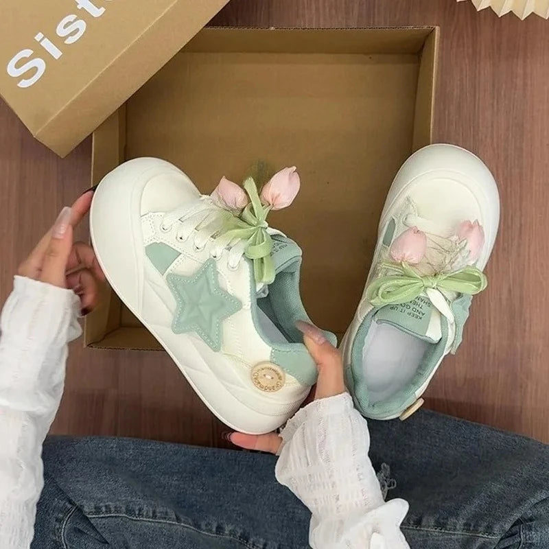 White sneakers with decorative elements held in front of a cardboard box.