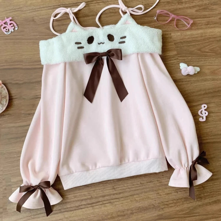 Pink blouse with cat face design and brown bows on a wooden surface.