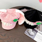 Two kawaii bunny hats, one pink and one black, with decorative strawberry elements on a wooden surface.