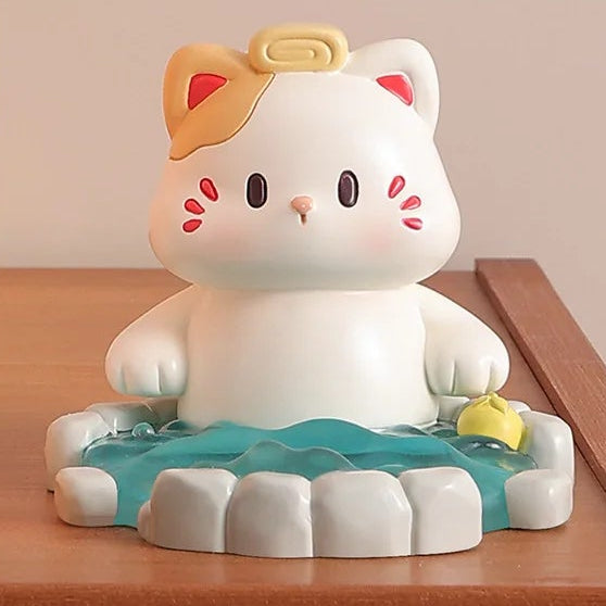 Cute resin figurine of a cat in a onsen with a yellow towel on its head on a wooden surface.