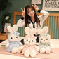 woman sat on the bed displaying the Miss Usagi Plushies different designs, one comes in white and blue another comes in white and pink and finally one comes in white a green.